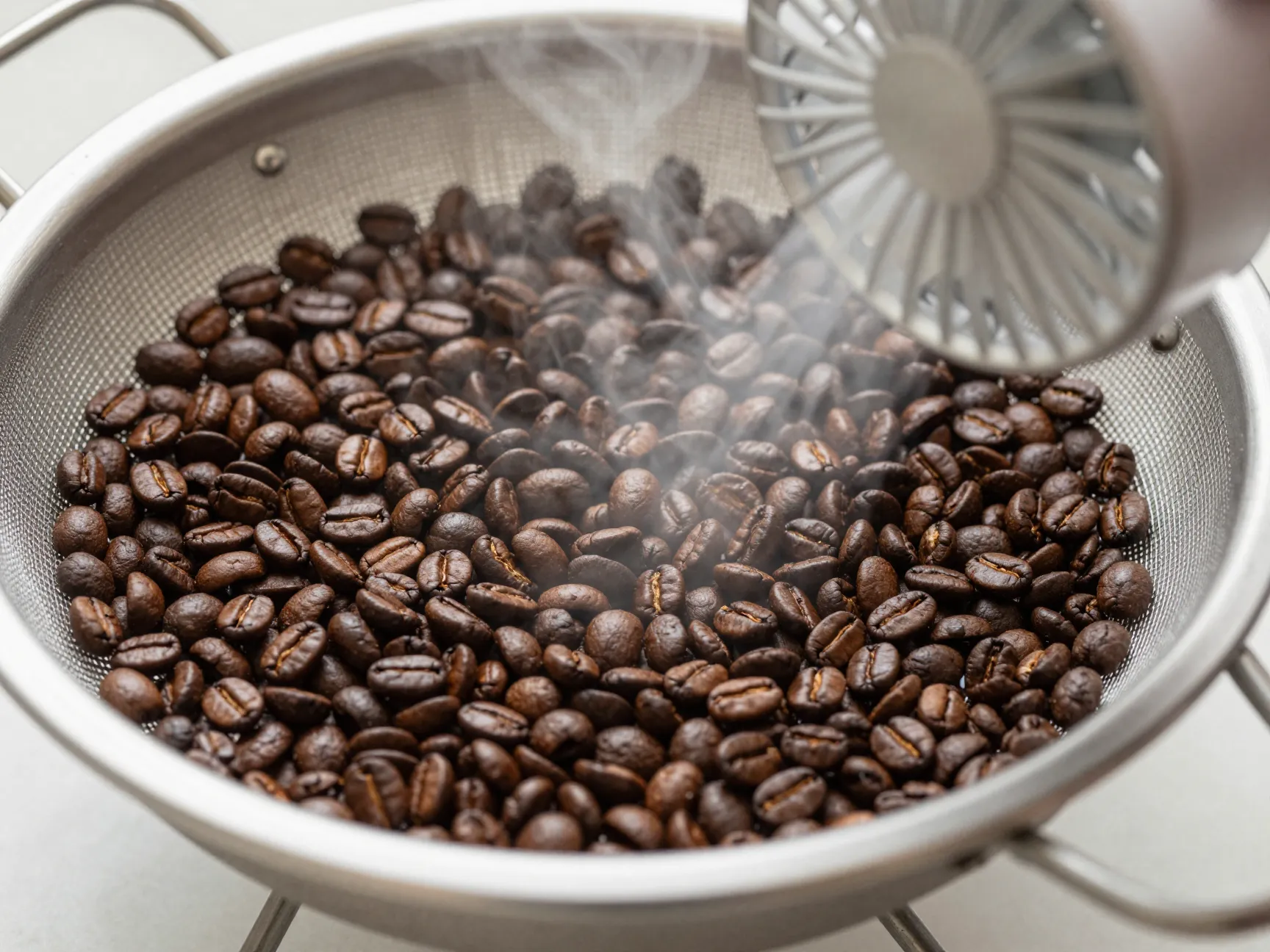 Freshly roasted coffee beans cooling rapidly in metal colander with fan