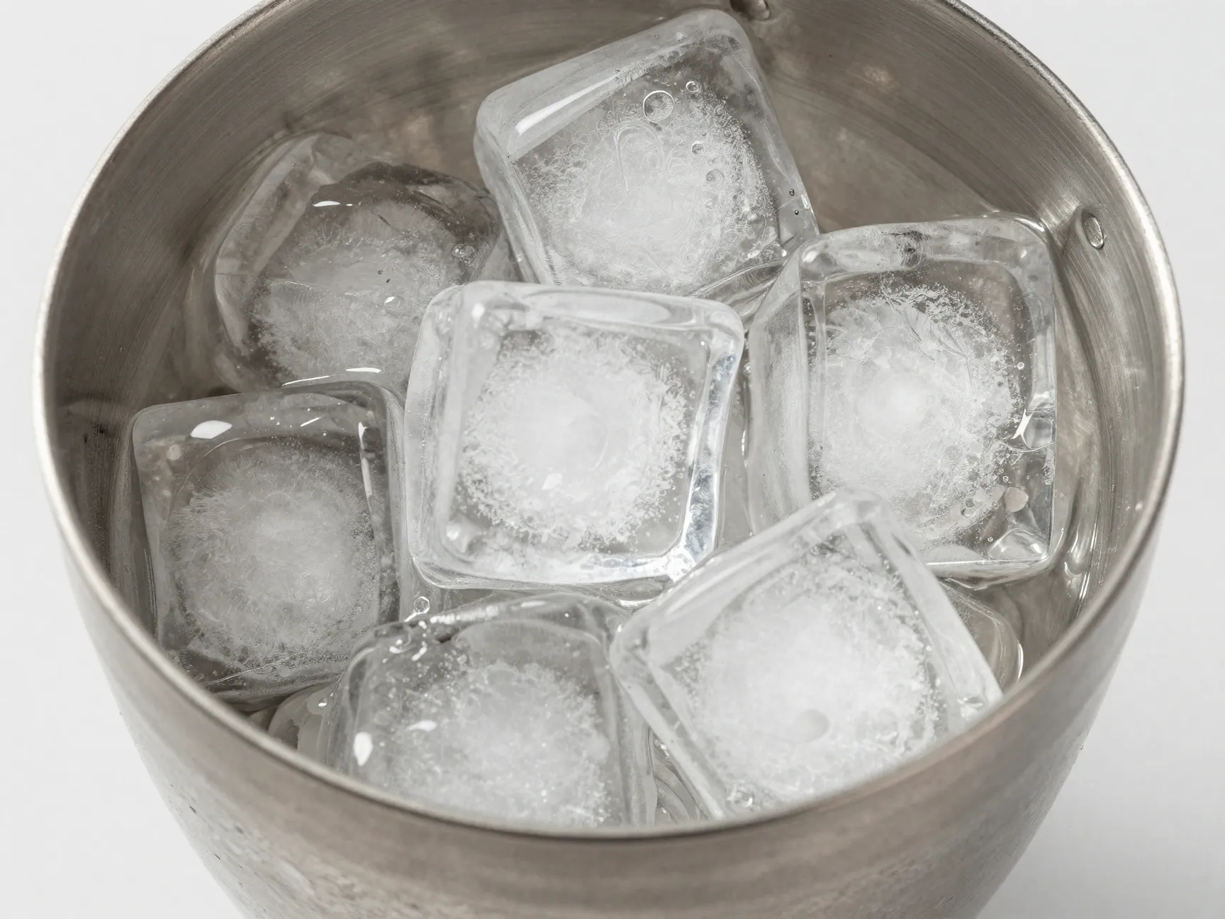 Large dense ice cubes filling a stainless steel cocktail shaker