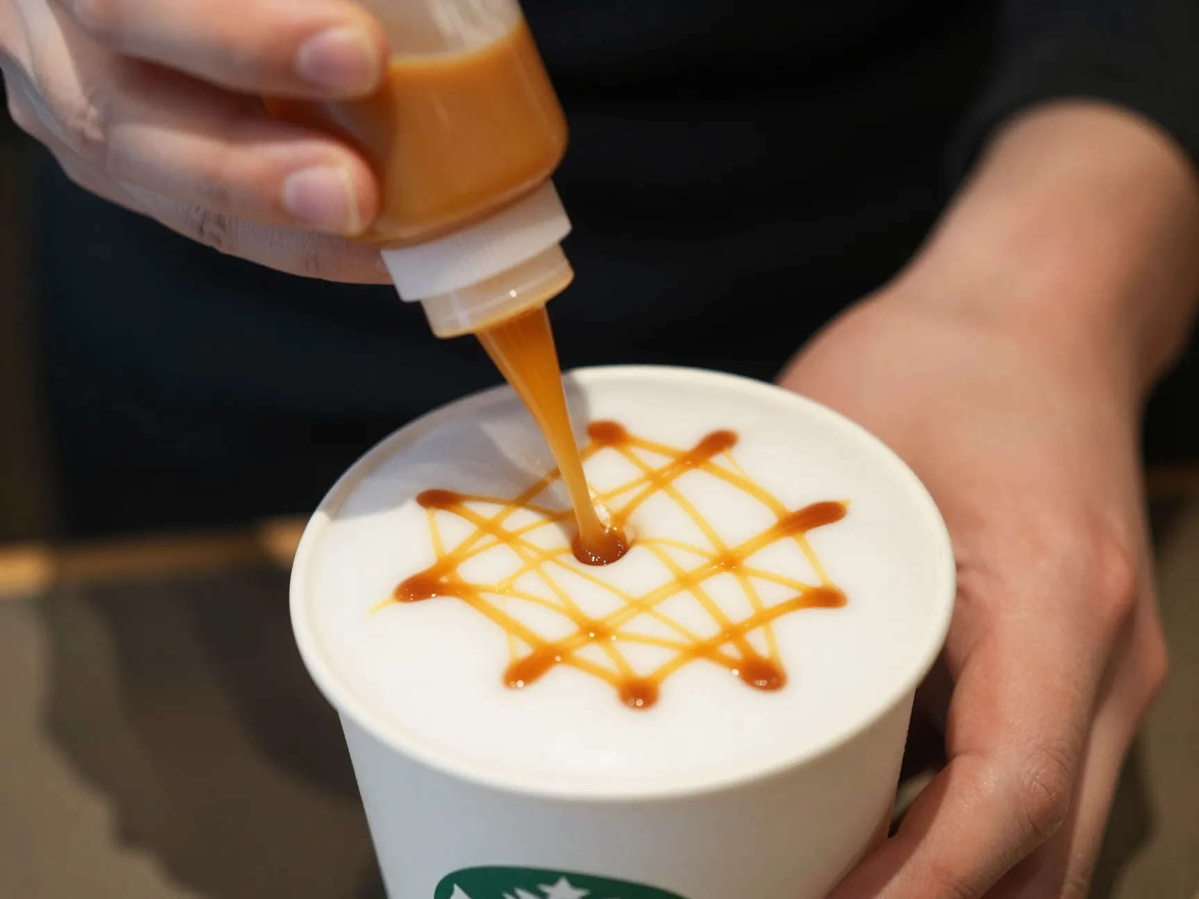Barista hand drizzling caramel in crosshatch pattern on foam