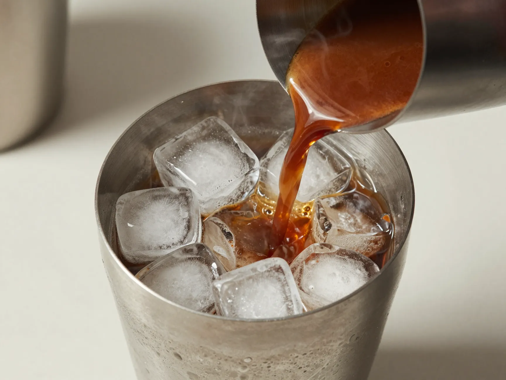 Warm espresso pouring into cocktail shaker over ice
