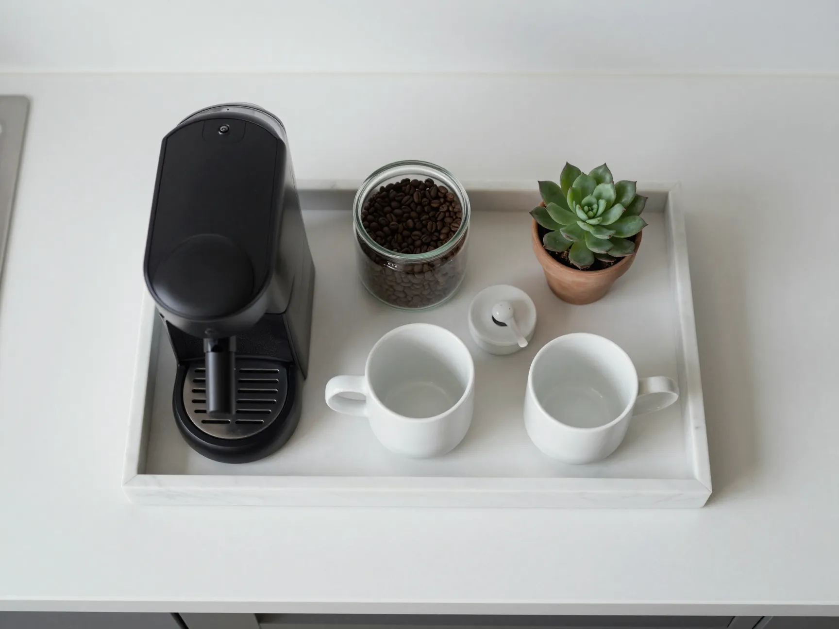 A marble tray on a kitchen countertop holding a compact coffee setup