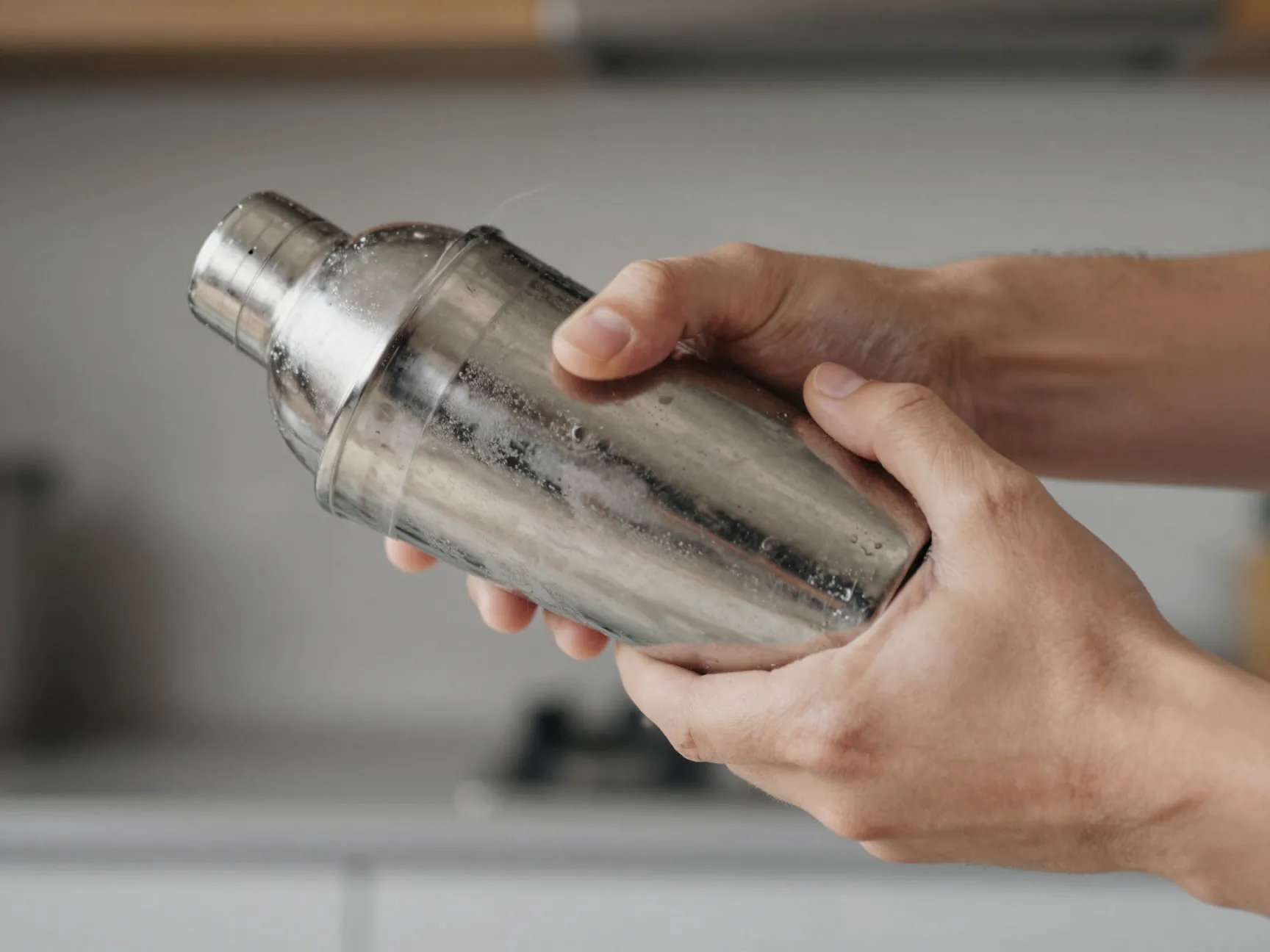 Hands vigorously shaking cocktail shaker horizontally