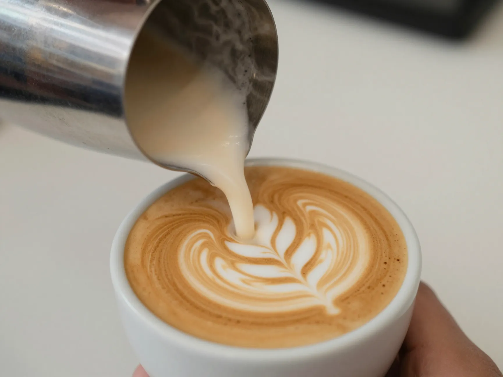 Milk pitcher pouring latte art into espresso cup