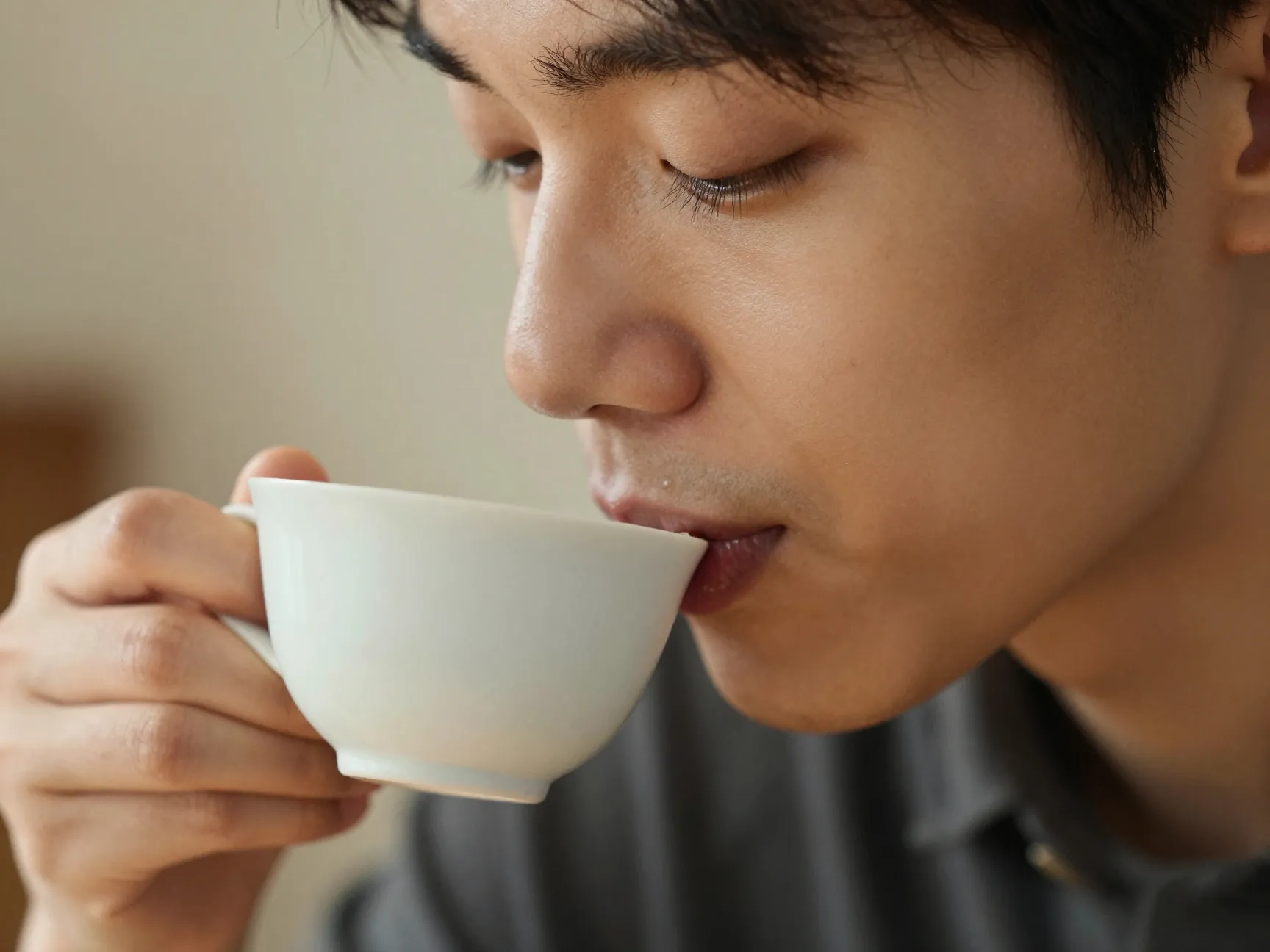 Person intentionally tasting black coffee from a small ceramic cup