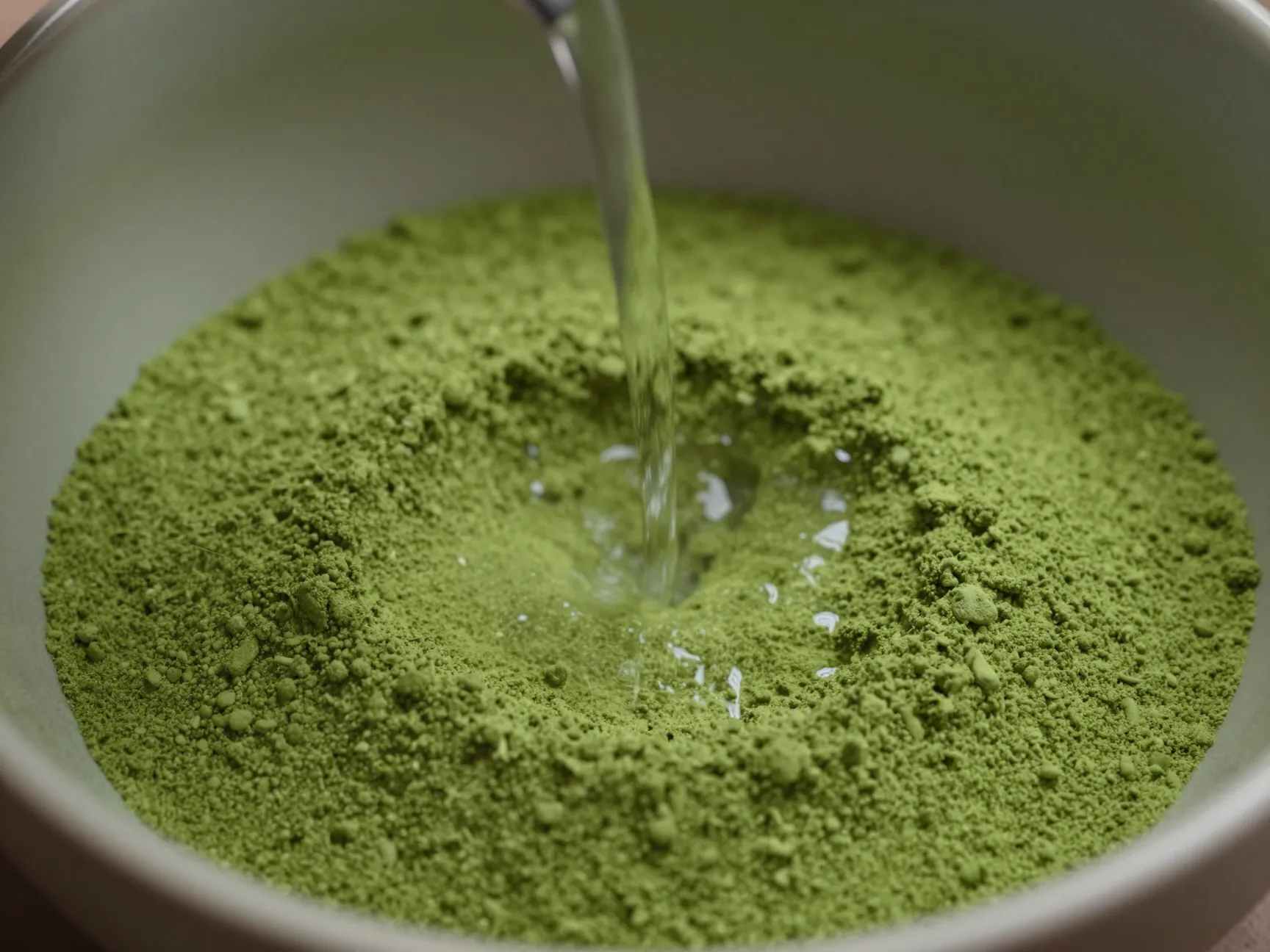 Initial small pour of hot water onto sifted matcha powder in bowl