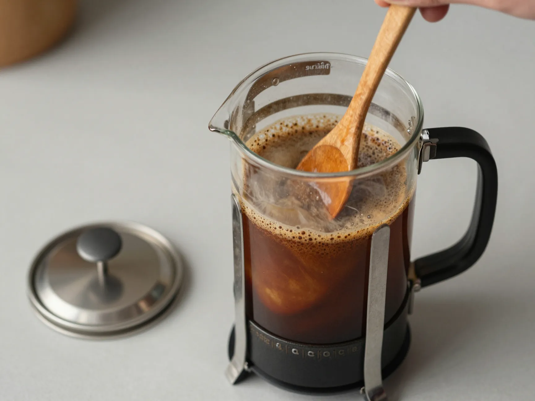Wooden spoon vigorously stirring coffee slurry in a french press