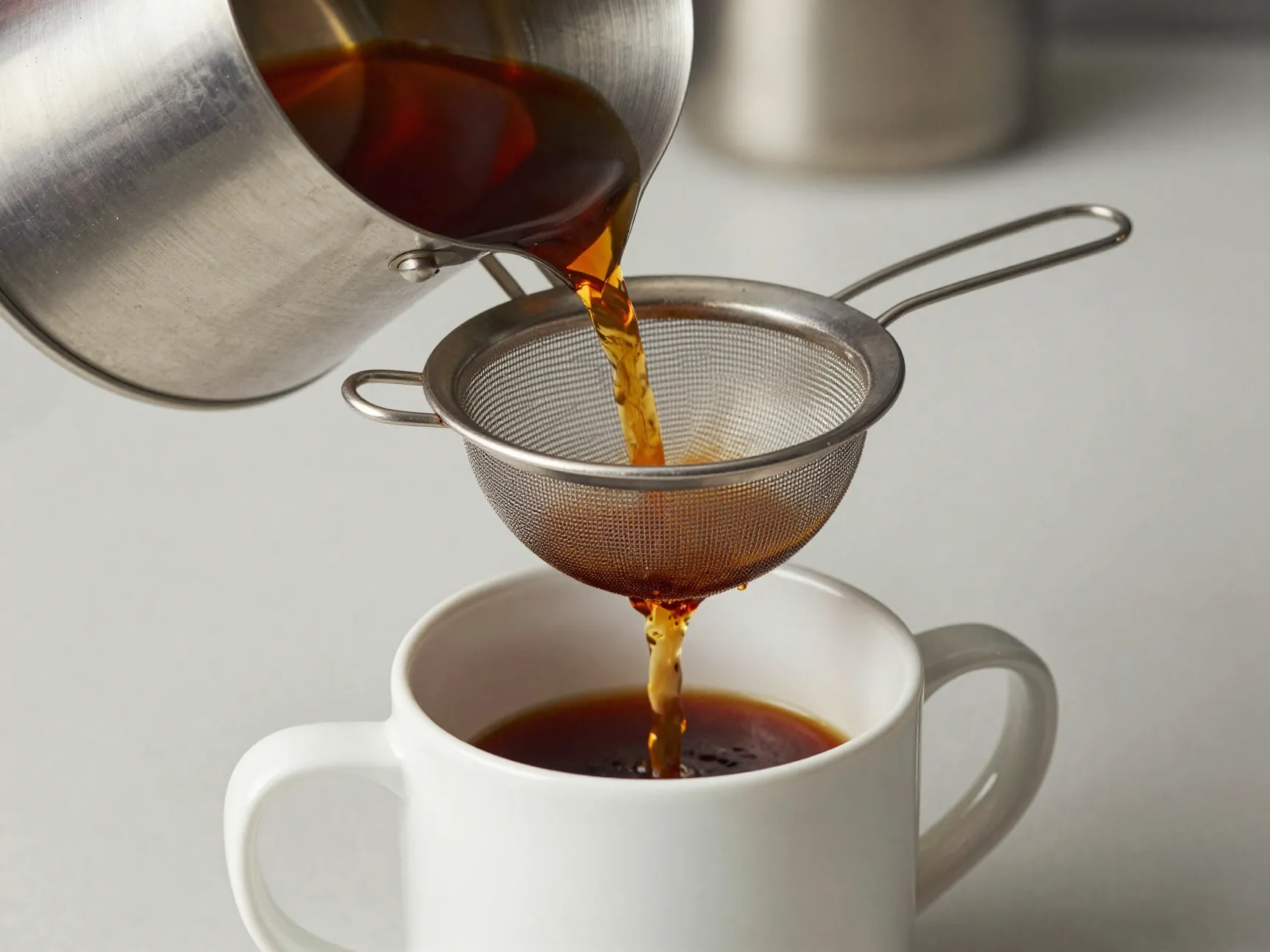 Sieve mesh strainer filtering coffee from saucepan to mug