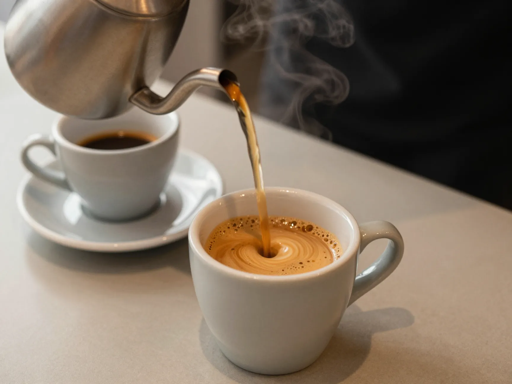 An americano coffee with hot water being poured into espresso