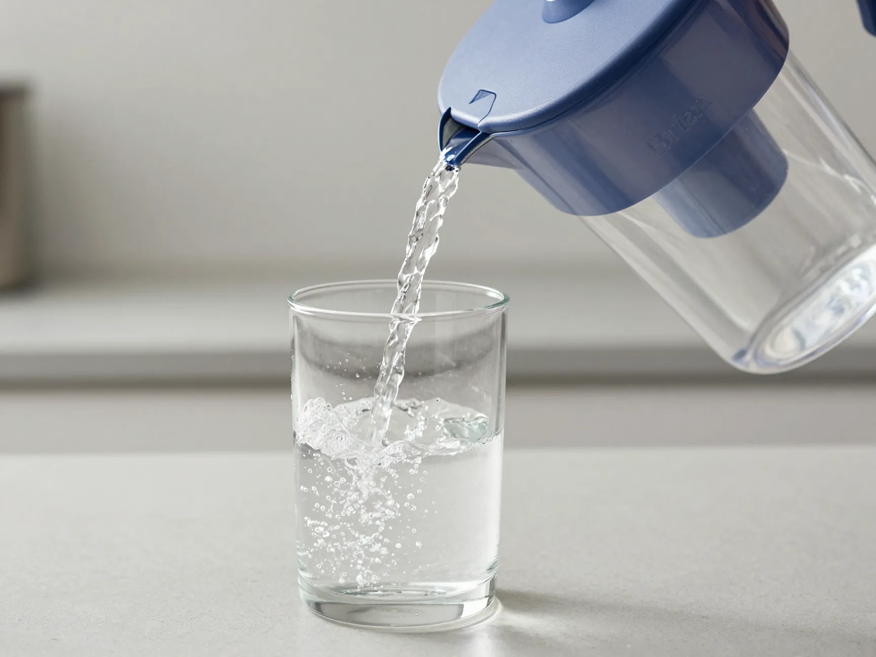 Filtered water pouring from brita pitcher into clear glass carafe