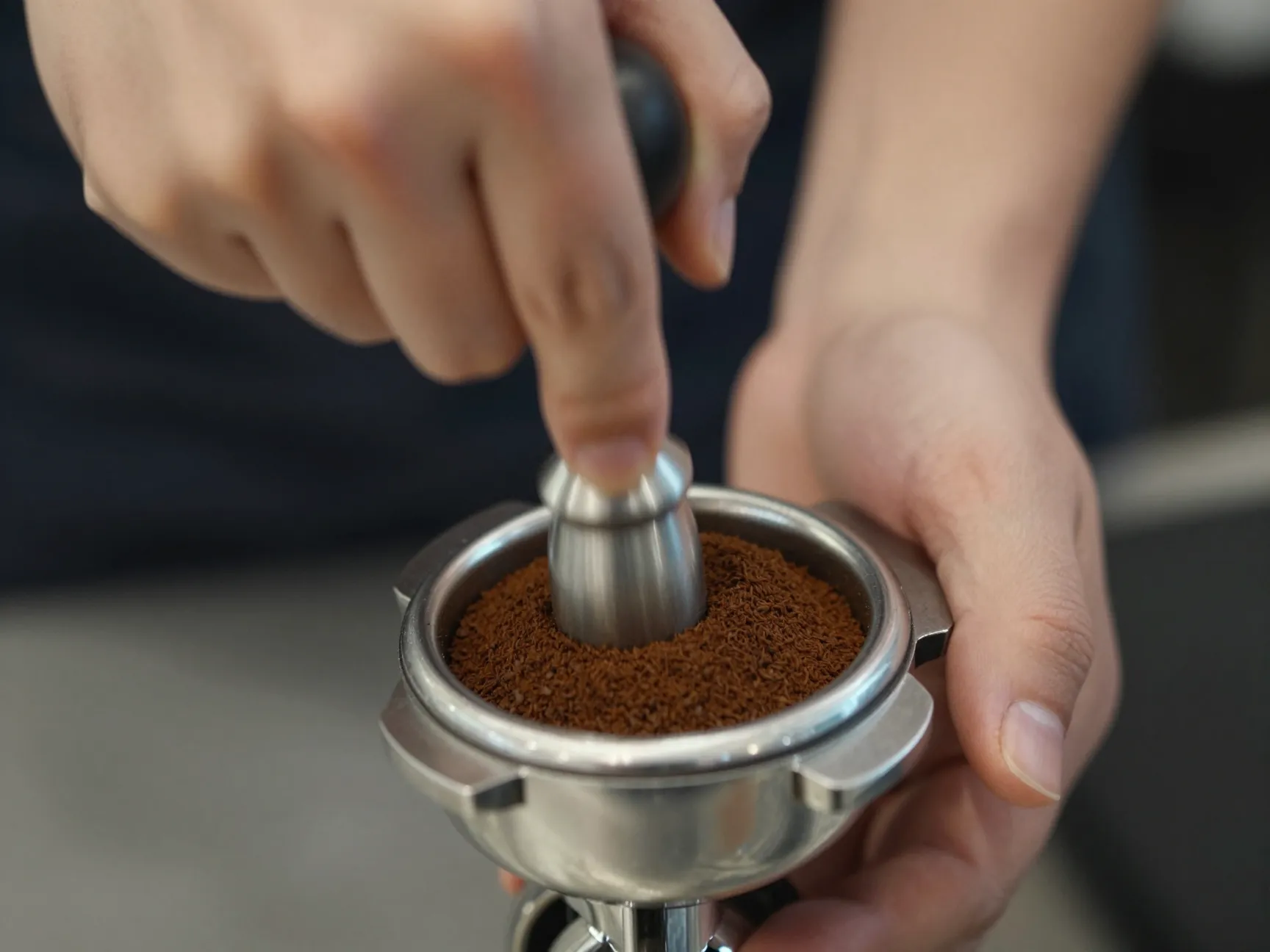 Barista hand tamping coffee grounds with even pressure in portafilter