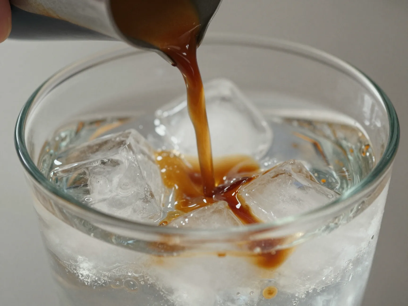 A slow gentle pour of espresso into a glass of iced water