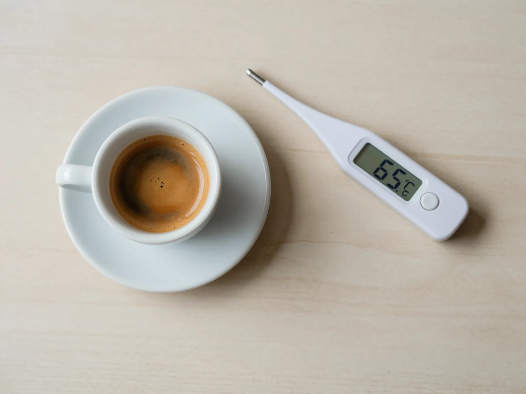 Espresso shot cooling on counter next to digital thermometer