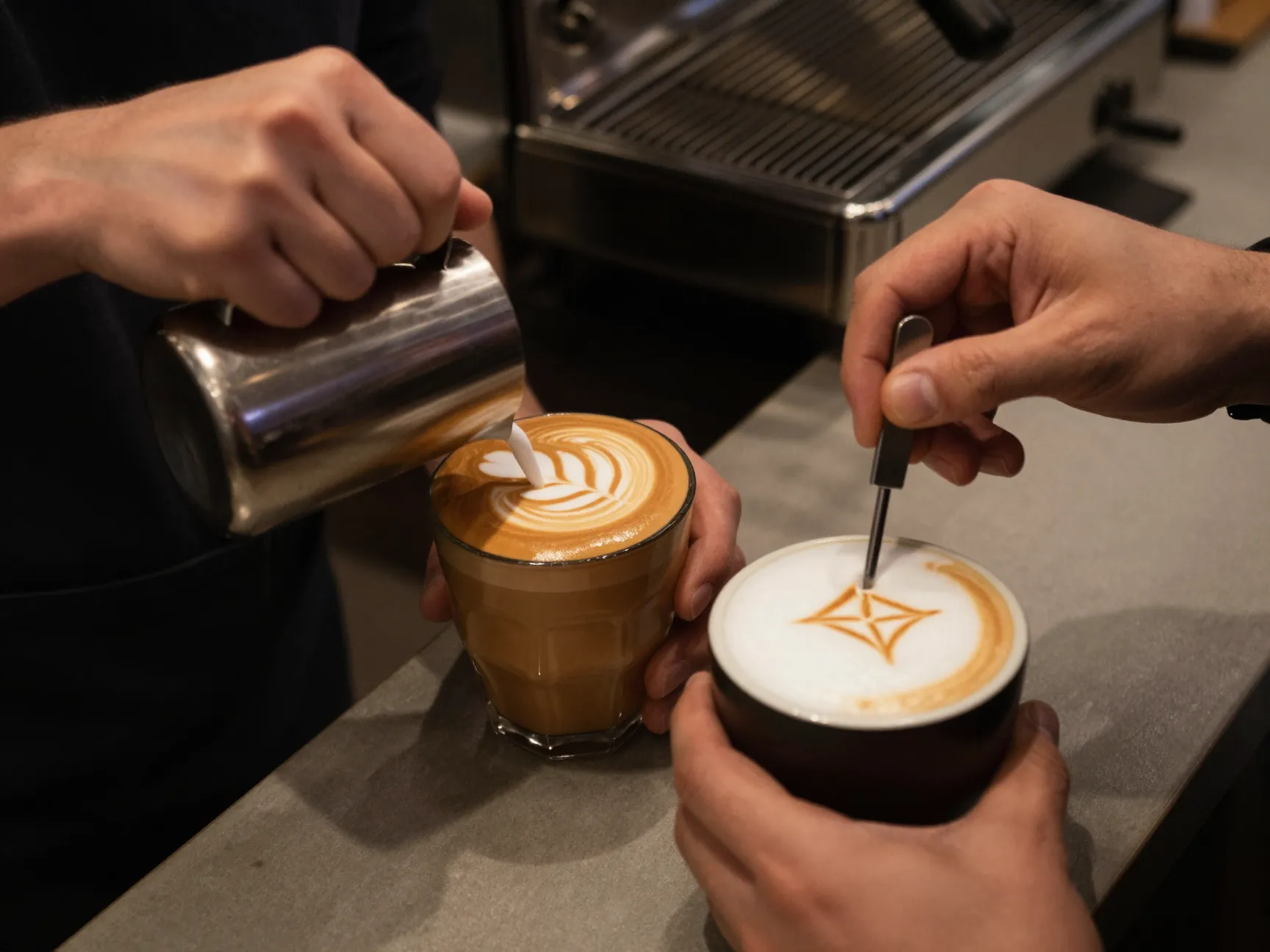 Barista pouring intricate latte art rosetta versus etching cappuccino foam
