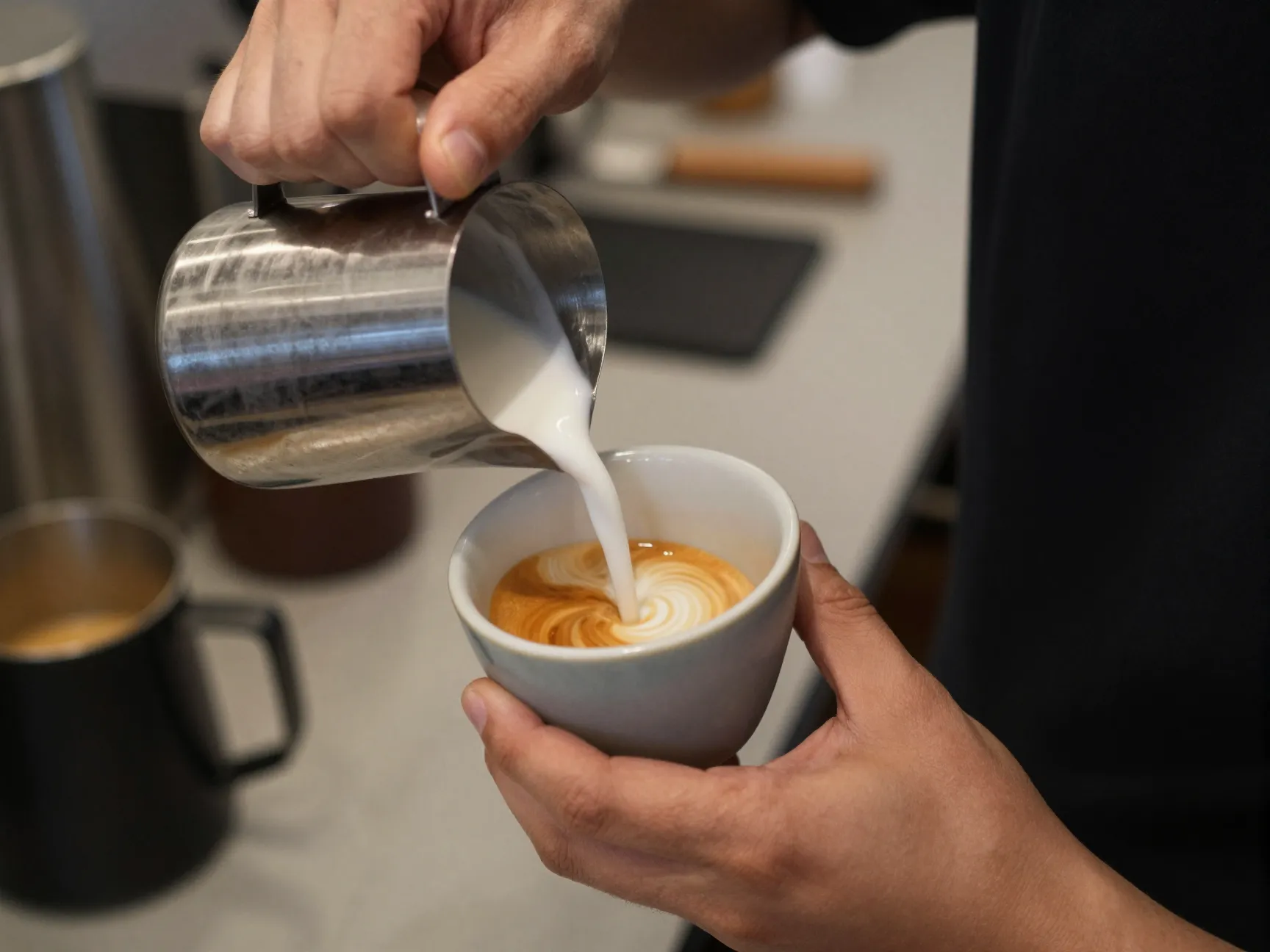 Barista pouring steamed milk into small ceramic tulip cup